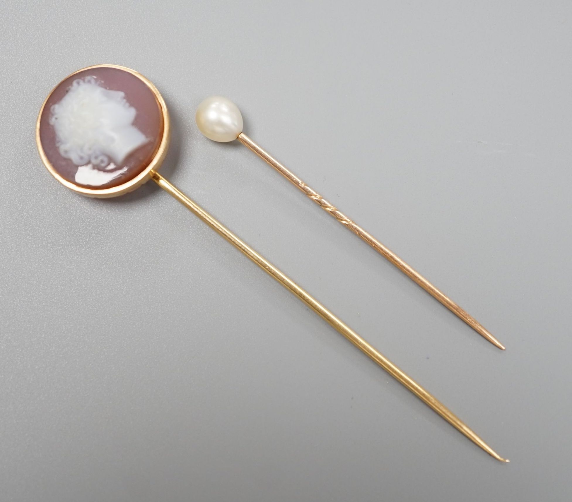 An early 20th century yellow metal and sardonyx cameo set stick pin, carved with the head of a lady to sinister, 79mm and one other cultured pearl set stick pin, gross 6.3 grams.